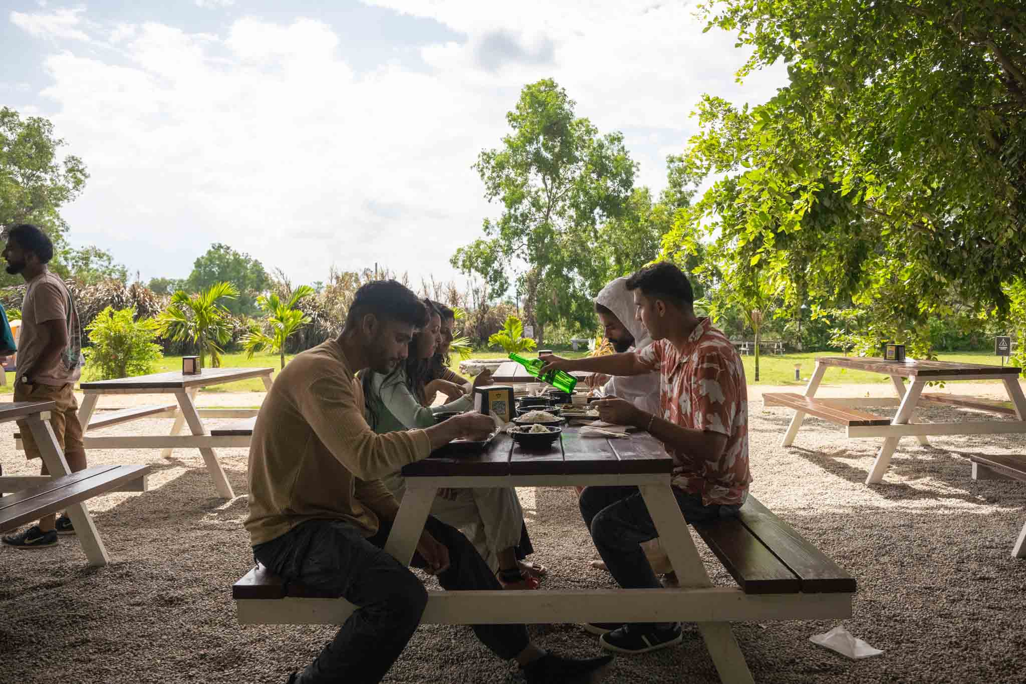 Friends eating together at a shaded picnic bench during daytime at the campsite